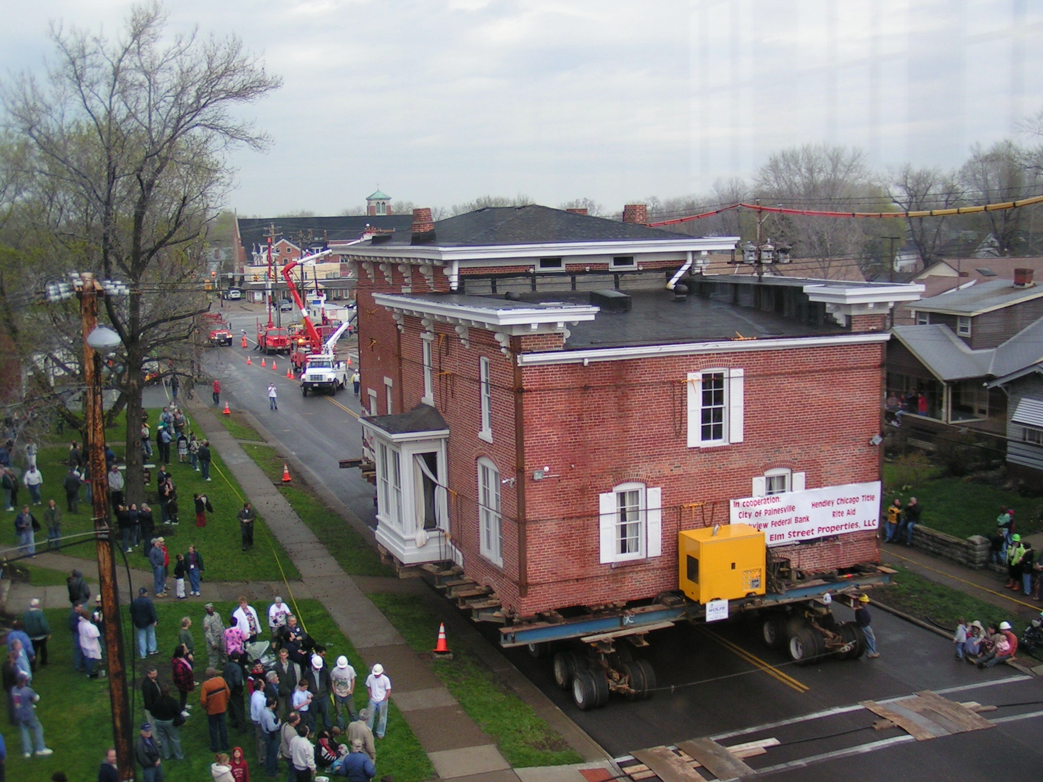 Historic Gage House lifted on dolly moving through streets on dolly with by standing crowd.