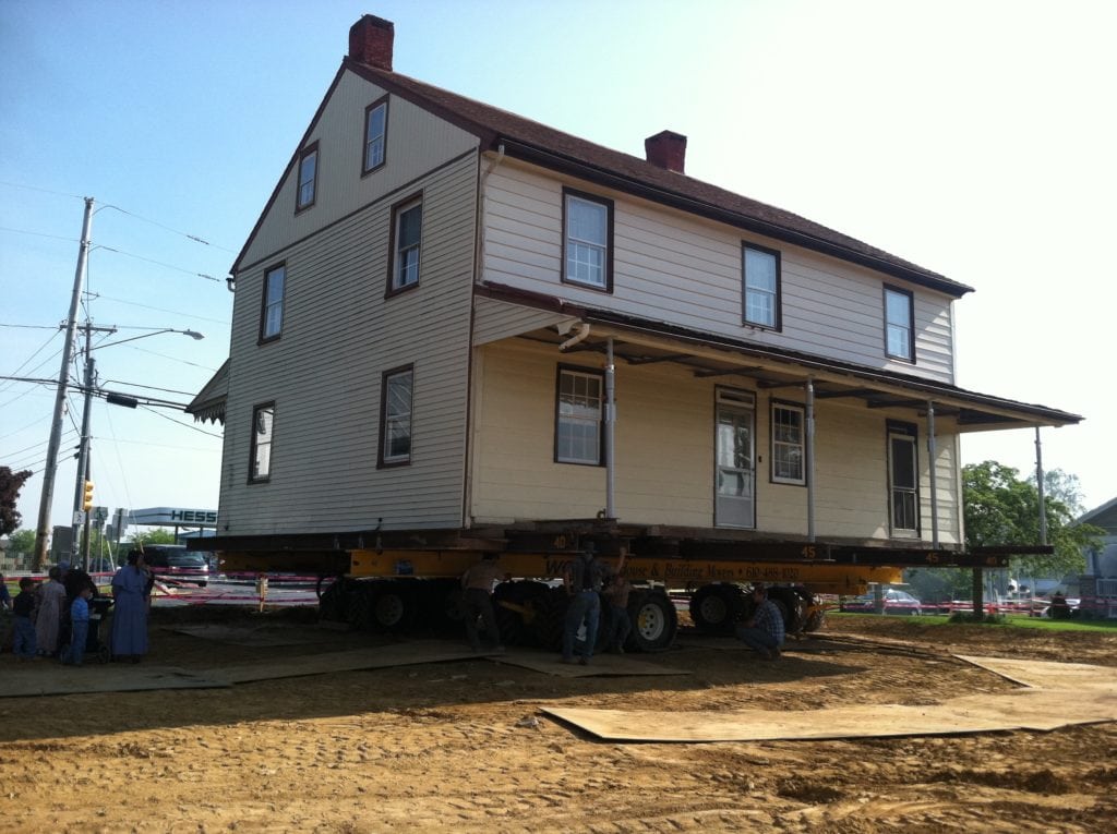 Two story lebanon house raised on dolly next to hess has station.