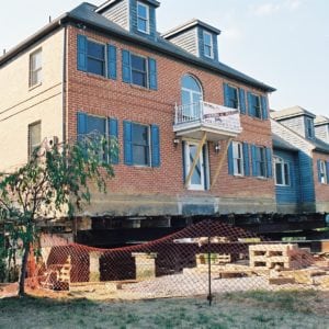 Two story brick house raised on wooden supports.