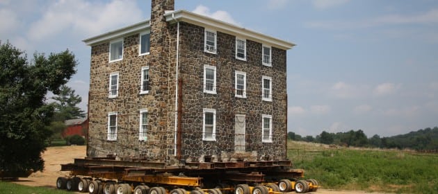 Three story stone house braced by chains moving on dolly.