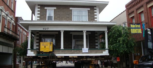 Two story stone house moving on dolly through tight city streets.