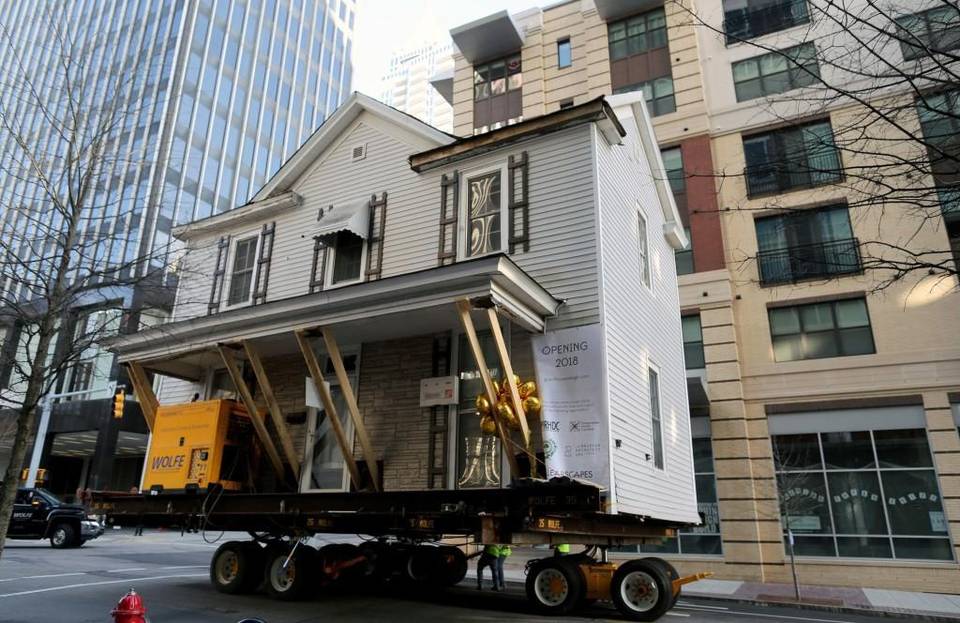 Two story historic house raised on dolly moving through city streets.