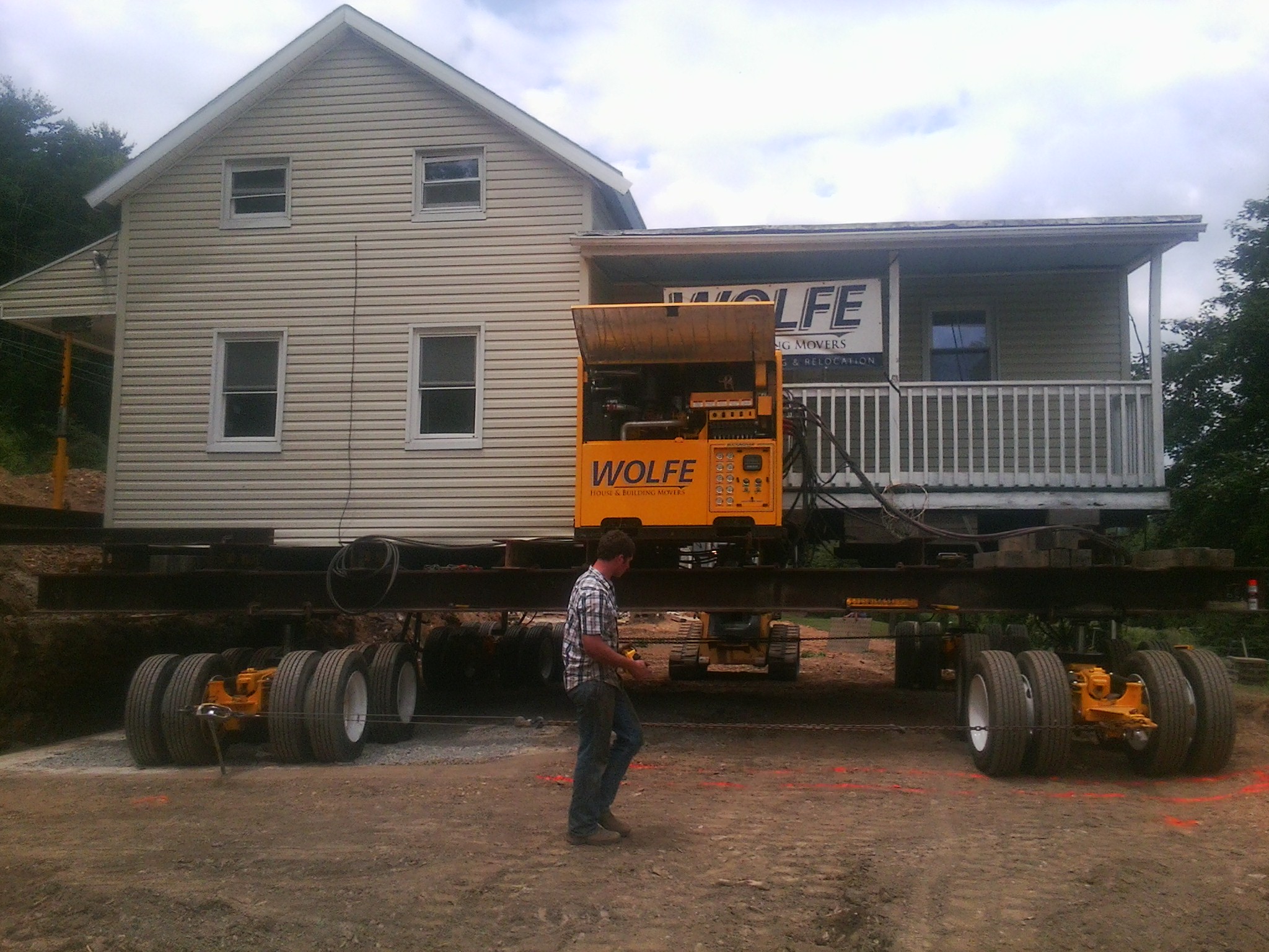 Tan farm house, with a balcony and an overhang, moving down a dirt road on a dolly system.