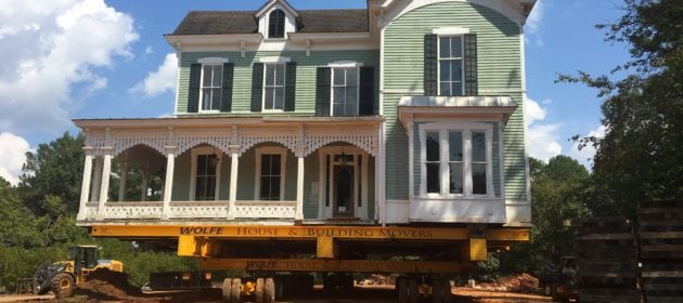 Historic southern style home moving on a dolly across packed earth.