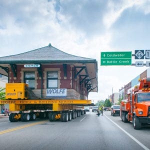 Sturgis Depot being transported on dolly through street of small town with utility vehicle parallel.