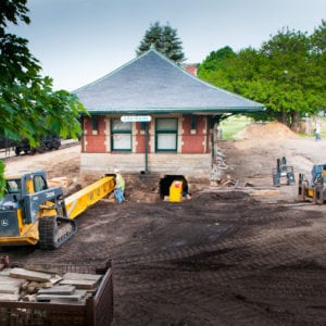 Yellow, steel beams being carefully maneuvered into place under the Sturgis Railroad depot by a skid loader.