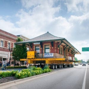 Sturgis Depot being transported on a dolly up a street through a small town.