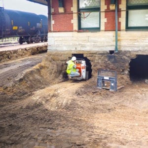 Worker riding mini skit loader into a tunnel dug under the foundation of a building.