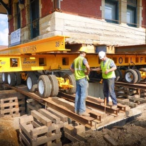 Workers examining measurement next to an old style train station lifted on a dolly.