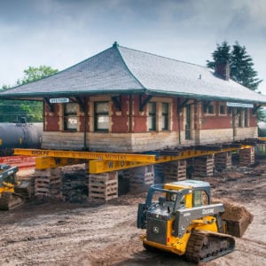 Sturgis Railroad depot lifted on supports with skid loaders excavating underneath.