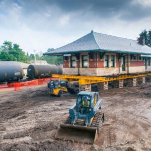 Sturgis Railroad depot lifted on supports with skid loaders excavating underneath.