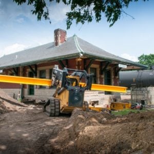 Skid loader carrying steel beam towards sturgis railroad depot under construction.