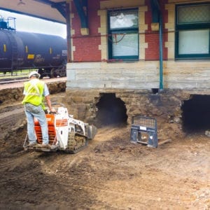 Mini skid loader backing away from entrance made in foundation to underneath space of depot.