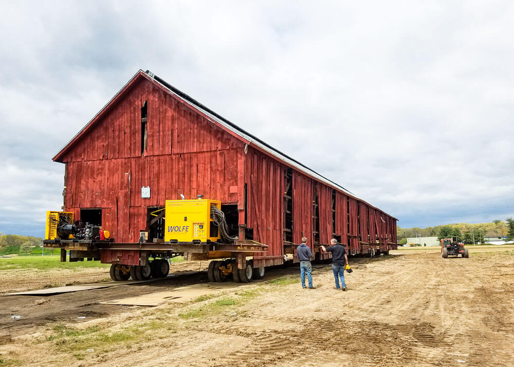 Wolfe employees drive a red tobacco barn across a field