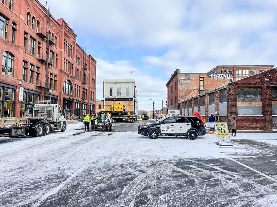 A police car blocks the street as a brick building is driven down it