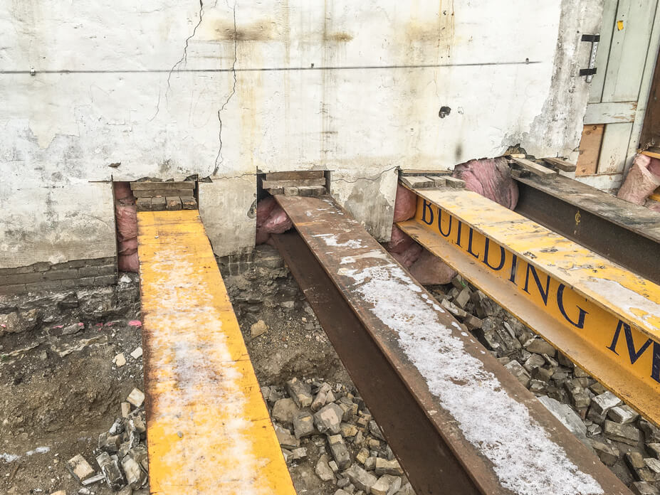 Steel beams are set under a brick wall for support