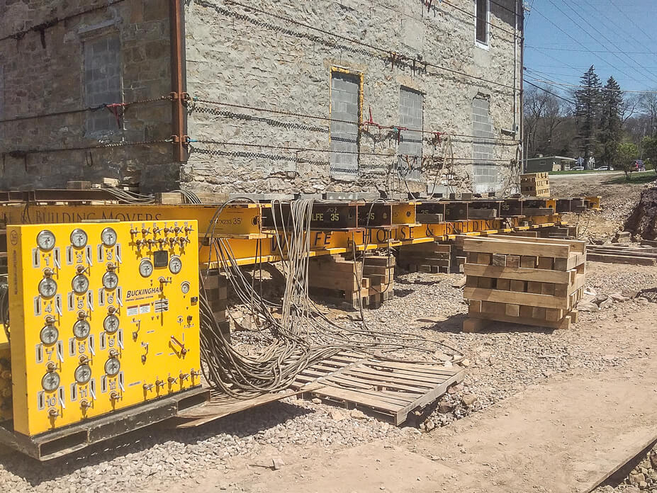 A unified jacking machine is hooked up to crib jacks to lift the stone house