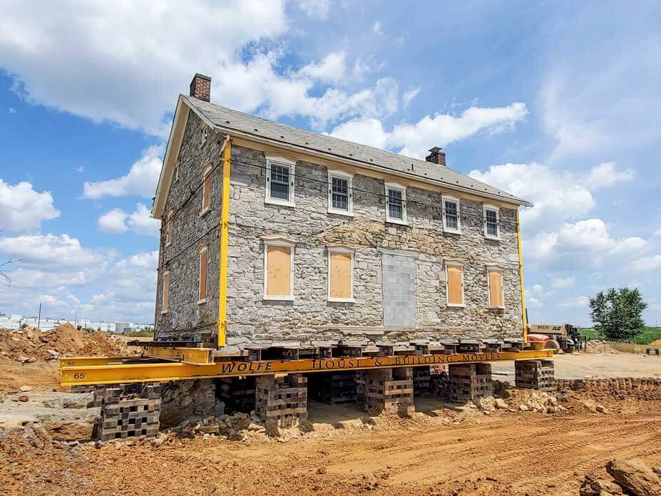 Stone house rests on cribbing and steel prior to relocation