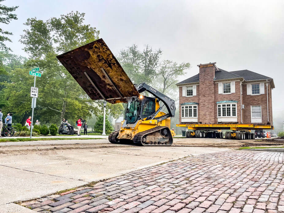 A skidsteer moves steel plate in front of the May House