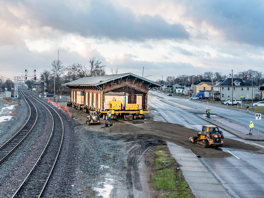 An aerial view of the single-story Hamilton Depot pulling out onto the road from its original location