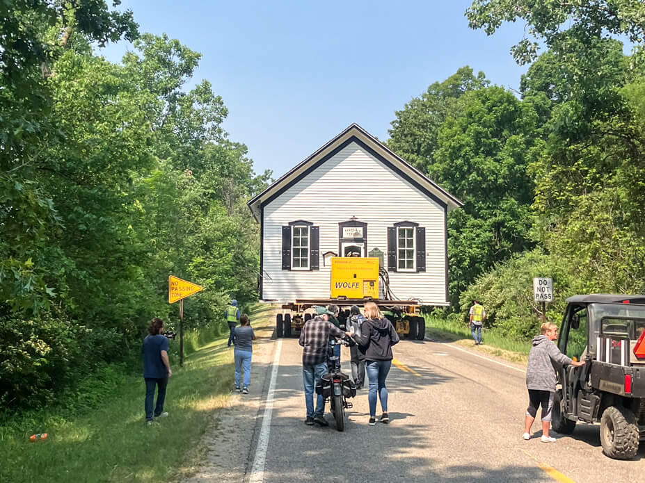 People walk behind the Tyrone Township Building as Wolfe moves it to its new location