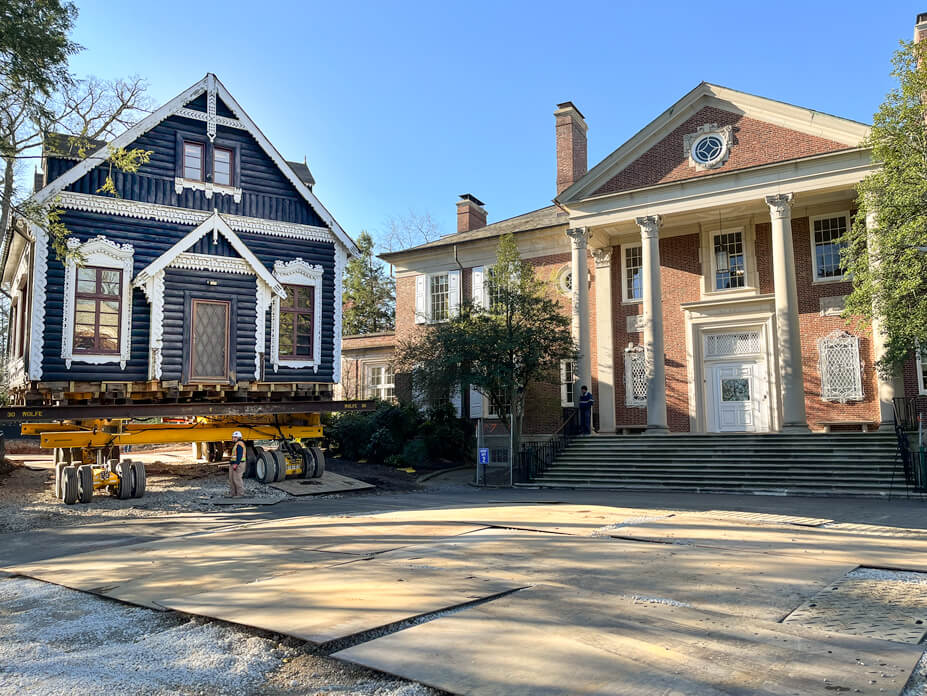 Dacha on Wolfe House Mover dollies and steel beams moves past a brick campus building