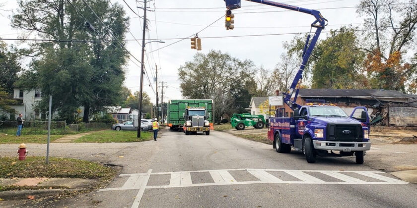 A utility truck lifts a power line so a semi hauling the Jackson house can pass under it