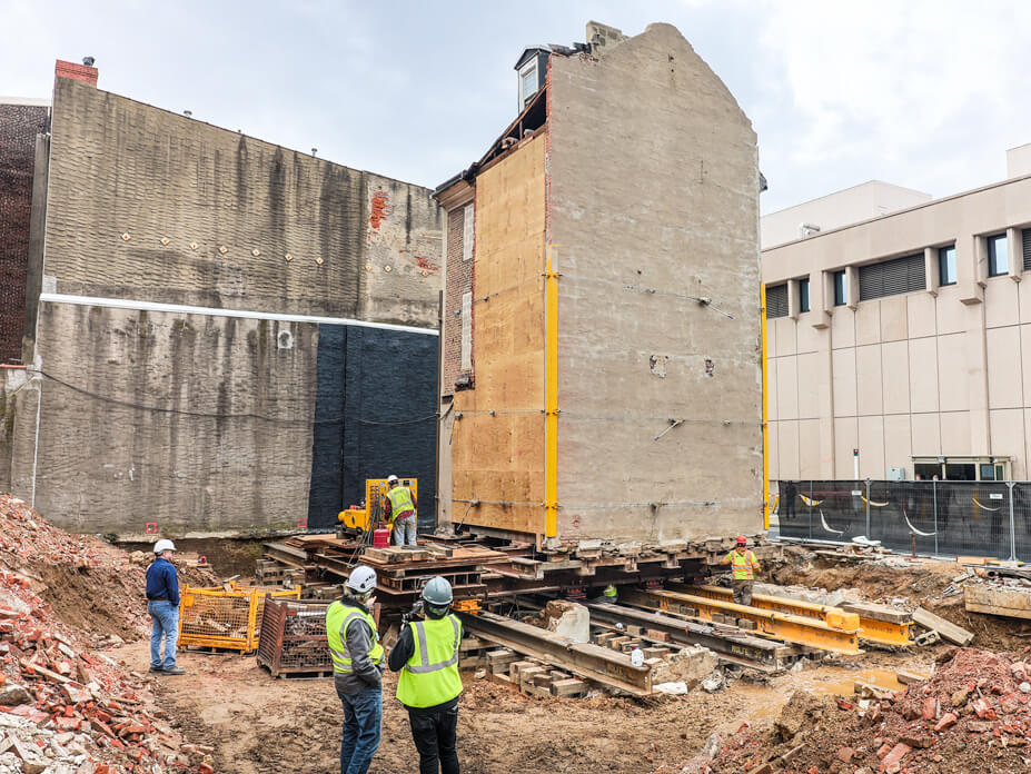 Workers look on as Wolfe foreman slides brick house over steel beams