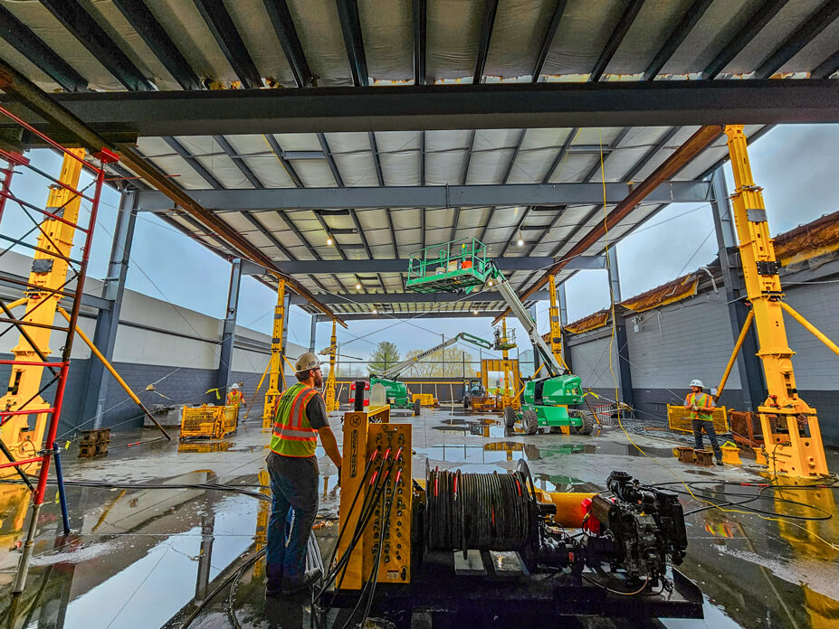 A Wolfe operator runs a Buckingham unified jacking machine with tower jacks to lift a warehouse roof