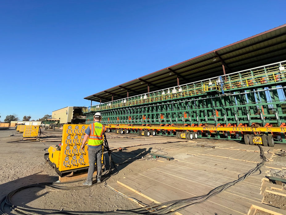 An operator runs a yellow unified jacking machine with lumber sorter on dollies in background