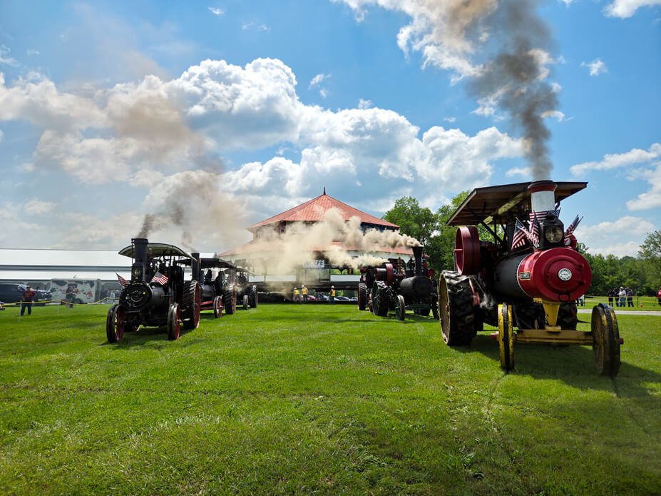 Two rows of historic steam engines line up in front of the carousel building