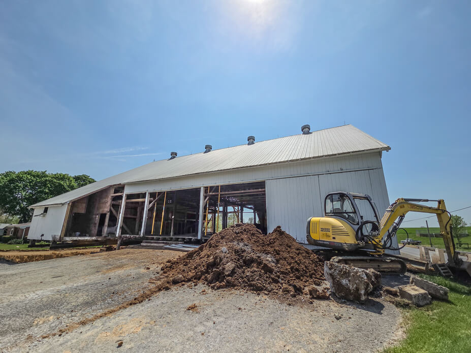 White barn with Buckingham jacking-shoring posts providing interior support and excavator with dirt in foreground