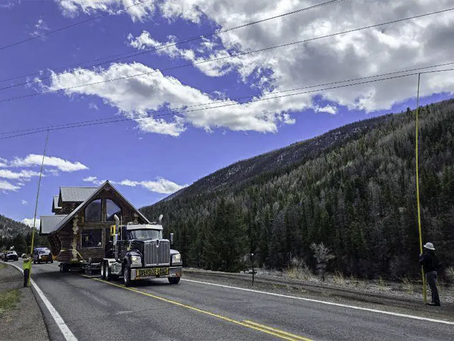 One of the log cabins being moved, and bucket trucks lifting wires